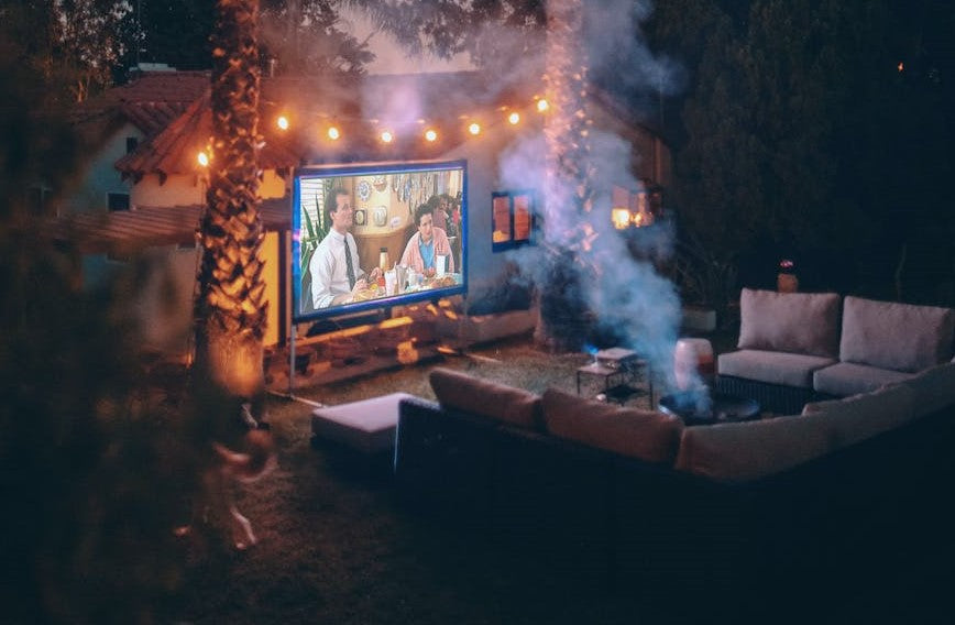 Person outside watching a movie on a big screen smoking 